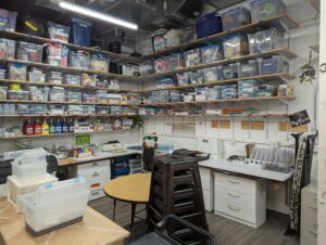 Many shelves full of clear plastic bins of makerspace materials. 