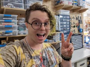Silly photo of Alison, MakerSpace Maven, posing in front of the electronics wall. 